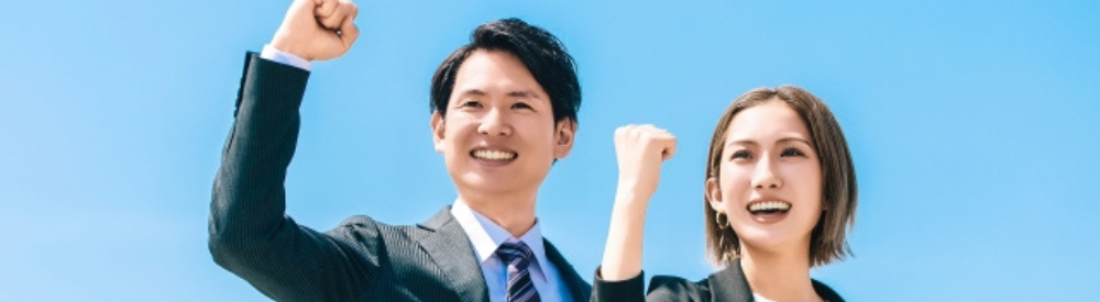 青空の下で拳を上げる若手不動産スタッフ